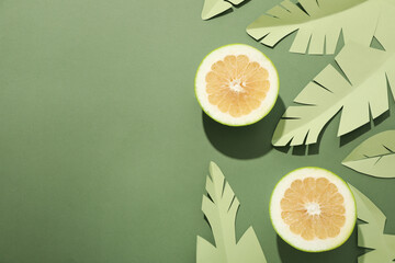 Sticker - Two half of pomelo fruit, paper tropical leaves on green background, space for text