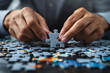 © Nano Photos - A person in a business suit assembling a puzzle on a table, focusing on fitting a single piece into place, symbolizing problem-solving and strategy.