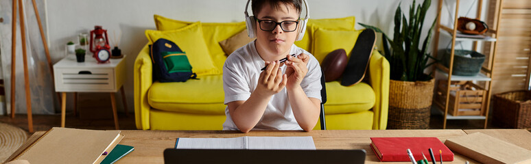 Wall Mural - A boy with Down syndrome with glasses works on his laptop at a desk.