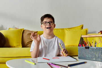 Wall Mural - A adorable boy with Down syndrome in glasses happily drawing on a yellow couch.