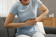 © New Africa - Woman suffering from stomach pain on sofa indoors, closeup