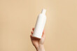 © Nastya - Hand holding white bottle of shampoo or hair conditioner on beige background, copy space