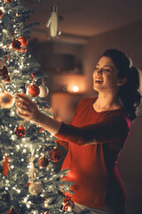 Wall Mural - A joyful pregnant woman decorating the Christmas tree with ornaments on Christmas Eve