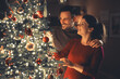 © Jelena - A lovely happy young adult couple decorating the shiny Christmas tree on Christmas Eve