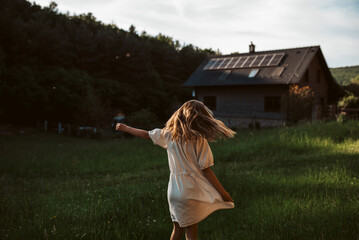 Wall Mural - Little girl in front of house with solar panels on roof, jumping, dancing and having fun. Concept of renewable resources.