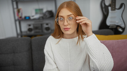 Poster - A stylish young woman adjusts her glasses in a modern living room, hinting at comfortable home life.