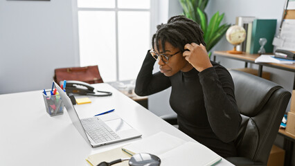 Sticker - Focused african american woman with dreadlocks working at her office desk with a laptop and notebook.