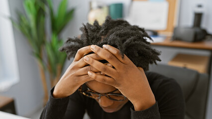 Canvas Print - A stressed african american woman with dreadlocks sitting in an office room, showing frustration or headache.