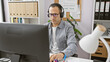 © Krakenimages.com - A focused man wearing headphones works at his computer in a modern office setting surrounded by shelving and a desk lamp.