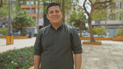 Sticker - A cheerful hispanic man with a backpack standing in a city park during daytime