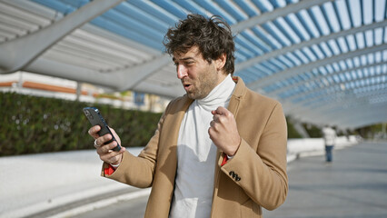 Wall Mural - Handsome hispanic man using smartphone in city park with architecture