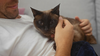 Wall Mural - Man holding a siamese cat lovingly in a cozy indoor setting