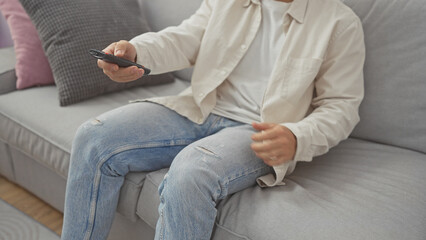 Poster - A young man relaxing on a sofa while holding a tv remote in a modern living room