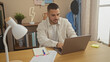 © Krakenimages.com - Hispanic man working from home using laptop at modern apartment's living room desk.