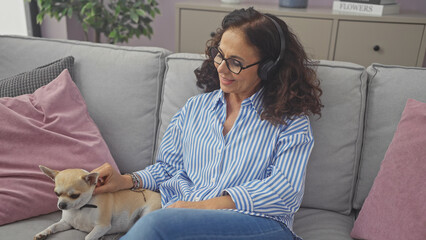 Canvas Print - Hispanic middle-aged woman relaxes with chihuahua on couch indoors, embodying a cozy home atmosphere.