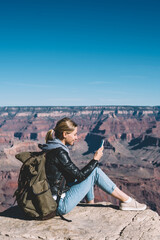 Wall Mural - smiling girl with rucksack using mobile connection for sending messages from rocky cliff in national