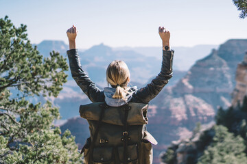 Wall Mural - Young hipster girl feeling victorious reaching destination during hiking in wild environment,back view of happy female tourist wanderer rising hands excited with beautiful nature landscape explore USA