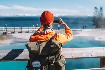Wall Mural - back view of female tourist with backpack using smartphone for taking picture of hot springs, hipste
