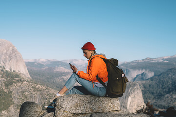 Wall Mural - young woman using mobile sitting on high rocks resting during hiking tour sending message,female tra