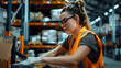 © Kiw11Fif - Focused Female Warehouse Worker in Orange Safety Vest Handling Inventory