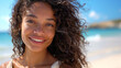 © Cadengo - A beautiful mixed race woman is smiling and posing on the beach, wearing casual linen with her hair in loose waves as she gently touches it under a clear blue sky