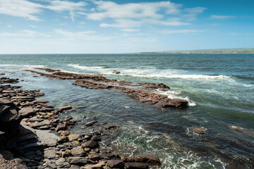 Wall Mural - The ocean is calm and the rocks are scattered along the shore. The sky is blue with clouds. Rough coastline of Ireland in county Clare, Warm sunny day. Nobody. Irish nature scene.