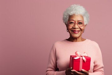 Wall Mural - Portrait of a glad afro-american woman in her 80s holding a gift while standing against minimalist or empty room background
