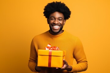 Wall Mural - Portrait of a blissful afro-american man in his 30s holding a gift on solid color backdrop
