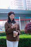 Fototapeta  - Stylish Woman with Coffee Browsing Phone in City
