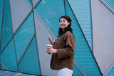 Fototapeta  - Stylish Woman with Coffee and Smartphone in Urban Setting