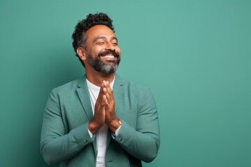 Wall Mural - Portrait of a joyful indian man in his 40s joining palms in a gesture of gratitude in front of solid pastel color wall