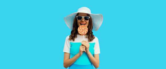 Wall Mural - happy cheerful young woman holding colorful lollipop wearing white summer hat on blue background