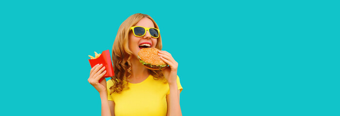 Wall Mural - Portrait of happy cheerful young woman eating burger fast food and french fries