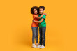 © Prostock-studio - Two African American children are embracing each other warmly on a vibrant yellow background. Their arms are wrapped around each other in a loving hug.