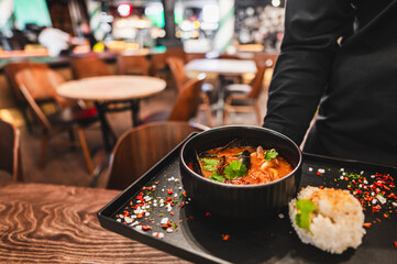 Wall Mural - A close-up view of a bowl of soup with garnishes, presented on a tray by a server in a restaurant setting