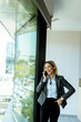 © BGStock72 - Young professional woman talking on mobile phone by office window on a sunny day