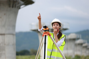 Portrait beautiful Asian construction engineer with a green safety vest hard hat and level survey camera.Engineer peering through a theodolite