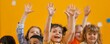 © Rattanathip - Group of happy children raising their hands in a classroom setting, smiling and engaged in learning activities.
