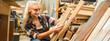 © chokniti - Attractive middle aged woman carpenter designer works with ruler, make notches on the tree in workshop. Image of modern femininity. Concept of professionally motivated women