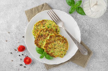 Wall Mural - Zucchini fritters or zucchini pancakes on a white plate with fresh basil and sour cream. Top view, selective focus.