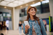 © Drazen - Happy female traveler with cell phone at airport looking away.