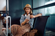 © Drazen - Happy female traveler texting on cell phone at airport.