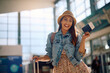 © Drazen - Happy woman holding her passport and plane ticket at departure area and looking at camera.