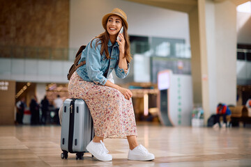 Wall Mural - Happy woman communicating on mobile phone while waiting for her flight at airport.