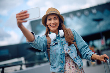 Wall Mural - Happy female traveler taking selfie at airport.