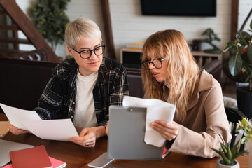 Coworking, colleagues, working at home concept. Two female students discussing working studying process using laptop doing paperwork in dormitory library. Distant learning at university college.