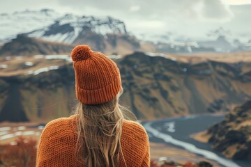 Woman in an orange sweater and beanie looks out over the mountains 