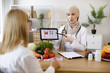 © sofiko14 - Mature lady patient visiting arabian woman nutritionist in hijab at modern clinic. Muslim female doctor showing on tablet graphs of food for healthy eating.