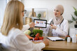 © sofiko14 - Professional nutritionist tells patient about benefits of healthy diet while holding tablet with graphs in hands. Arab female doctor makes treatment plan for gastrointestinal tract in modern clinic.