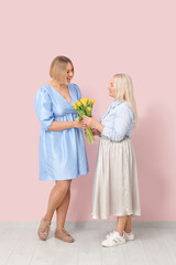 Poster - Adult woman with her mother and bouquet of tulips near pink wall. International Women's Day celebration